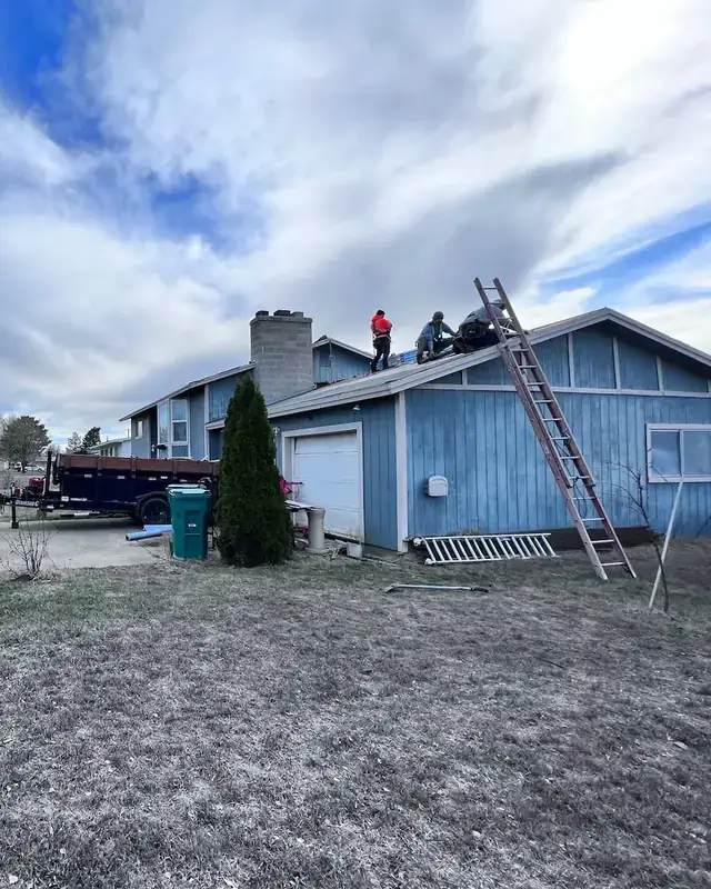A&A crew working on a blue house roof with a ladder against the eave