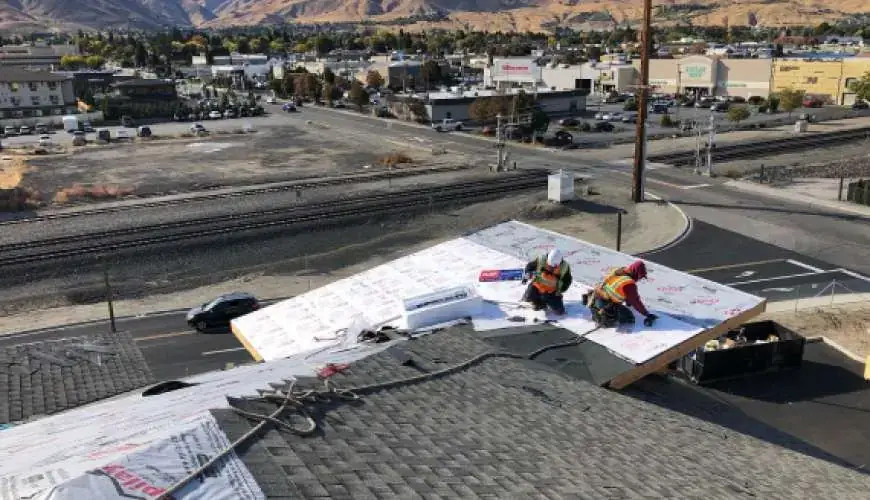 Two A&A roofers laying membrane on a commercial roof above a Tri-Cities street