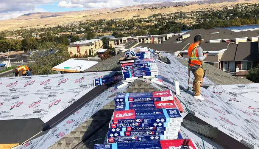 A crew member on a roof loaded with shingle bundles, a valley in view