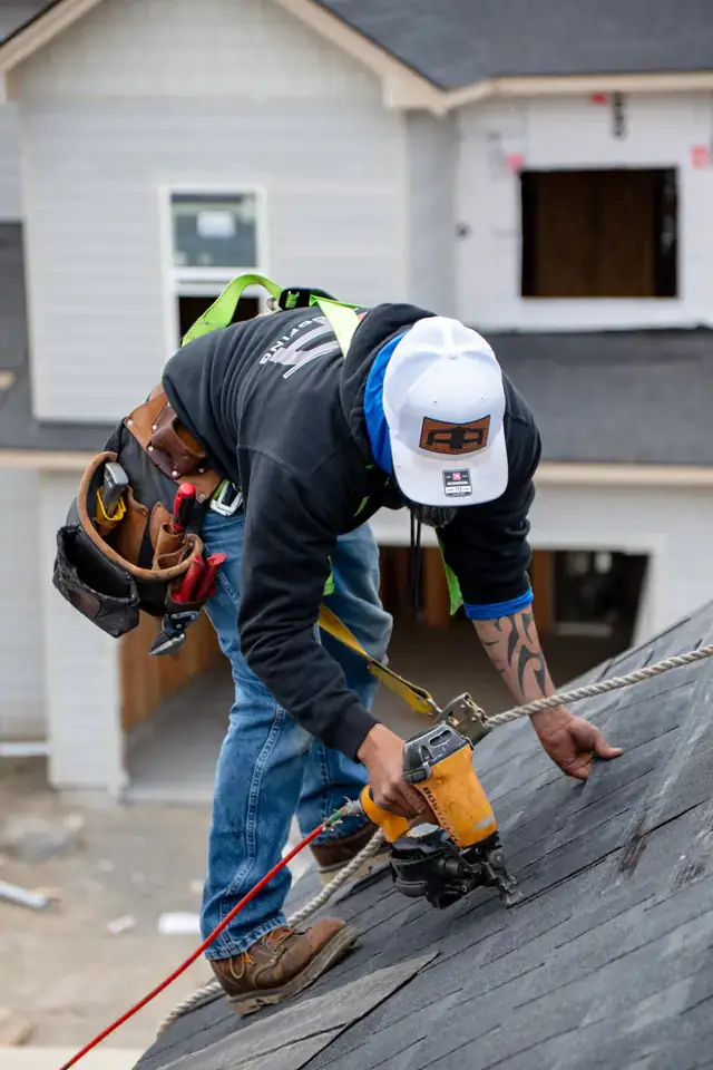 A crew member in a harness and A&A cap nailing shingles