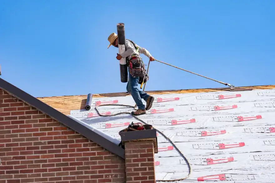 A roofer carrying a roll of underlayment across a deck on a brick home